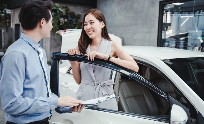 Smiling lady signed a document to pick up the new car from the dealer. Woman signs the document in order to pick up the car from the car rental. 
Concept for car rental.